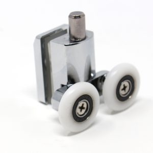 Close-up of an Insignia bottom-mounted spring-loaded shower door roller designed for Insignia shower cabins. The component features a robust, polished chrome-finish zinc alloy body containing a clamp for holding glass. A vertical cylindrical pin at the top acts as the spring-loaded mechanism to maintain downward tension and secure the door in the track. The base is fitted with two 24mm white nylon wheels featuring internal bearings, engineered for smooth, low-friction sliding in damp conditions. This replacement part is isolated against a white background.