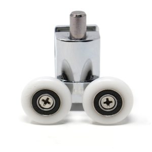 Close-up front view of a bottom-mounted spring-loaded Vidalux shower door roller assembly designed for Vidalux shower cabins. The unit features a durable zinc alloy housing with a reflective polished chrome finish. Two white 24mm nylon wheels are positioned at the base, each secured with a central Phillips-head screw and black bearing seal to ensure smooth, low-friction sliding. A cylindrical metal tension pin extends from the top of the body, part of the spring-loaded mechanism that compresses for easy installation into the bottom guide track. Isolated on a white background, this replacement part helps maintain door alignment in steam showers and hydromassage enclosures.
